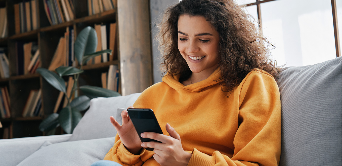 Kvinna siter i soffa med en mobiltelefon i handen